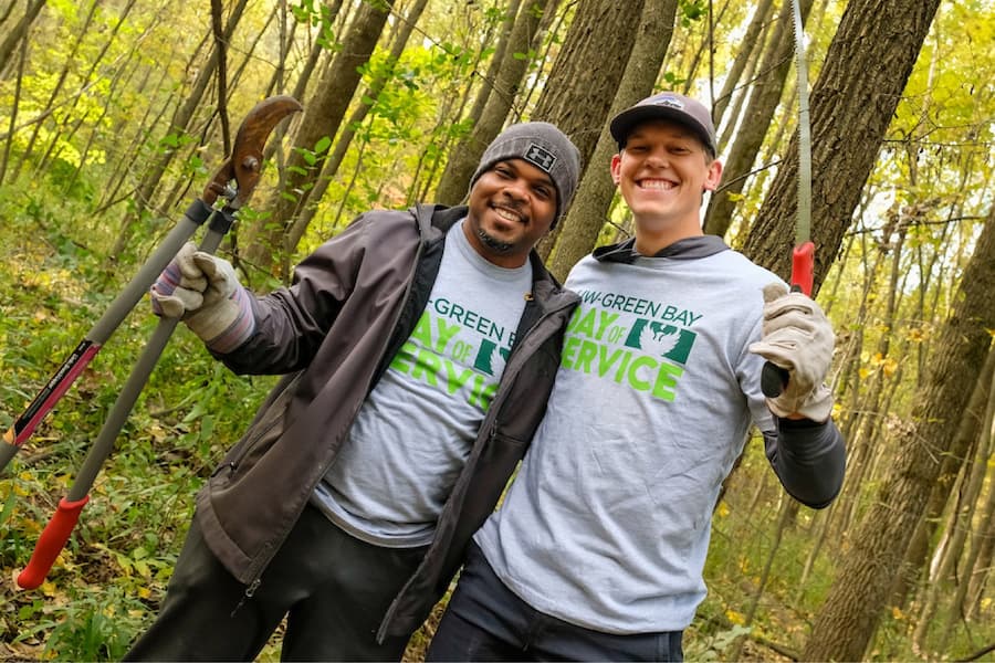 Two UW-Green Bay employees holding gardening tools in wooded area on Day of Service