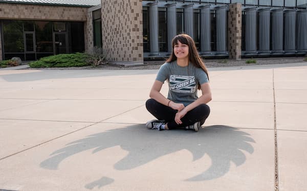 UW-Green Bay student seated in the sun casting a shadow that's the shape of a phoenix