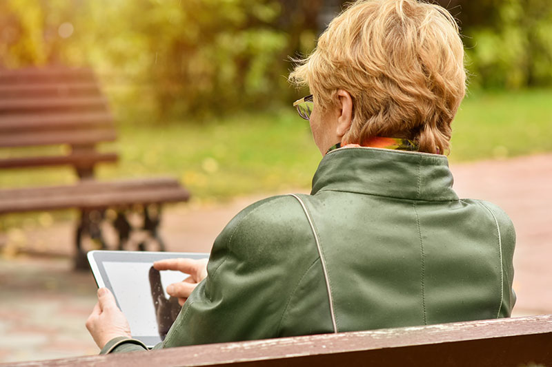 Mature woman sitting outside looking at tablet browsing class options