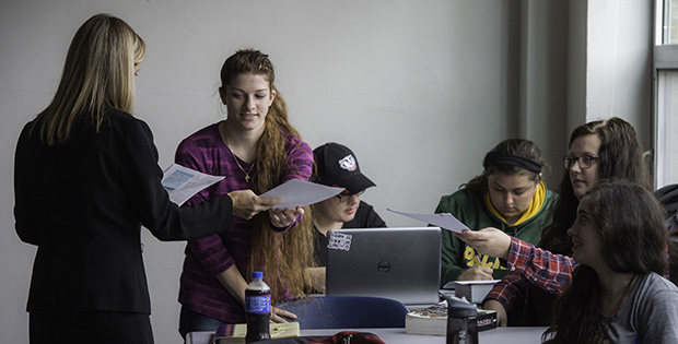 Students in a class passing papers and on computers