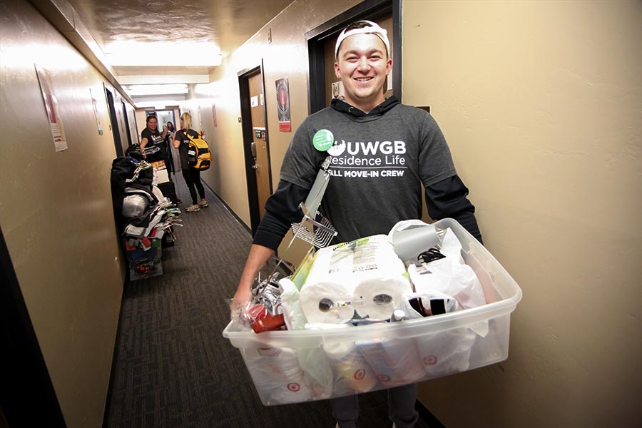 A move-in volunteer carrying a bin of cleaning supplies and shower shelf to a room