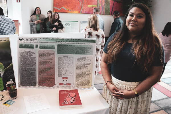 Student standing with research poster at the social work symposium