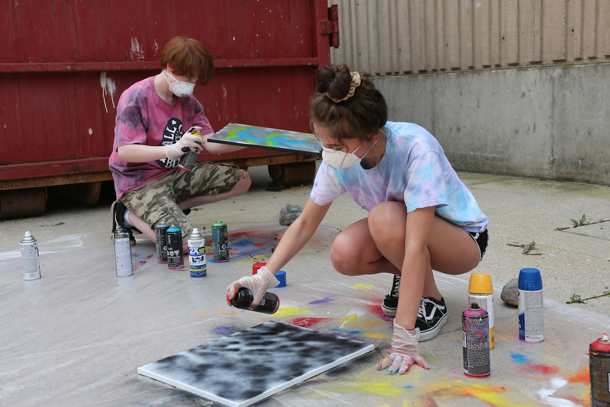 students spray painting a canvas
