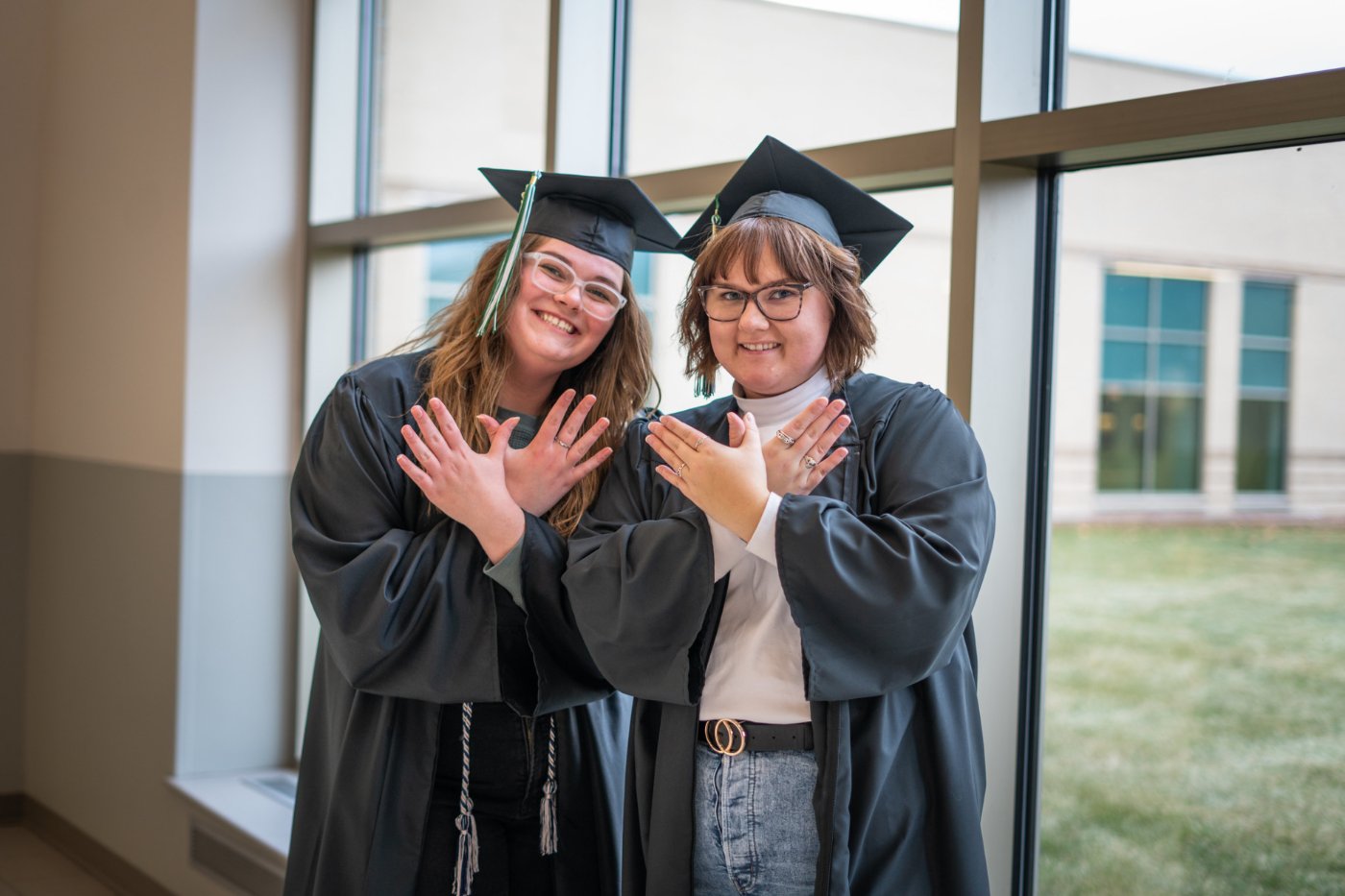 Two students, dressed in their caps and gowns, pose for a photo while creating the signature Phoenix hand gesture.