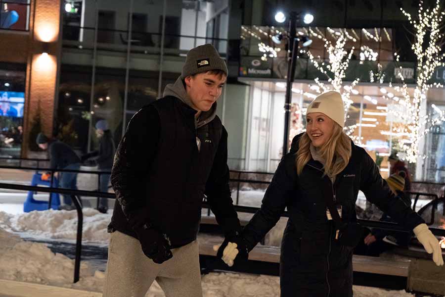 two students hold hands while ice skating at the Titletown ice skating rink.