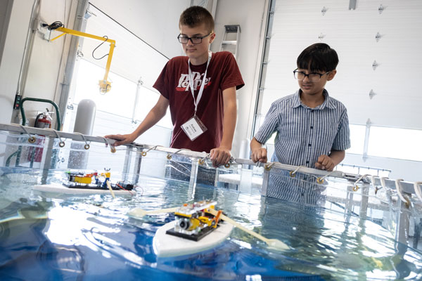 Two children test aquatic robotic boats in water 