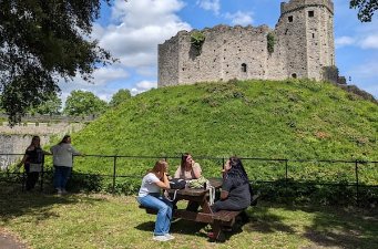 Students studying abroad in Whales sit at picnic table with castle in the background