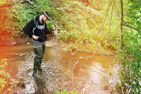 A UW-Green Bay manitowoc campus student does water research wearing hip waders in a stream