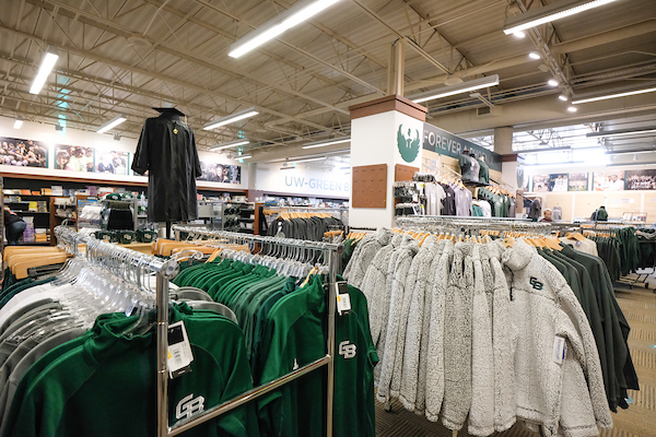 A few rows of UW-Green Bay Athletics apparel are seen in the foreground, with more apparel and merchandise in the background.