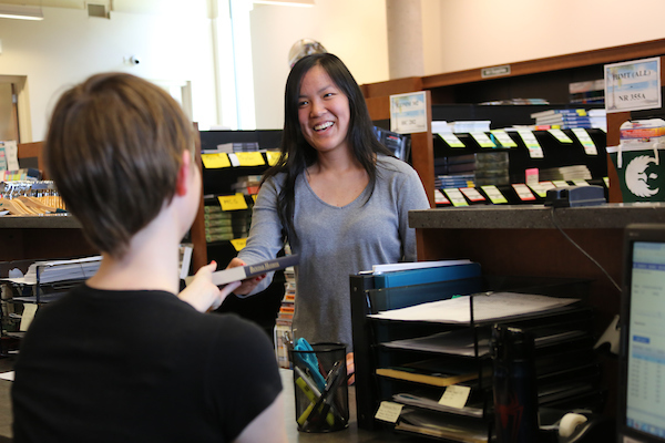 A Phoenix Bookstore employee hands a student their textbook from behind a checkout counter.