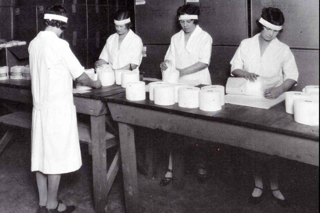 Black and white photograph of women in a factory wrapping toilet paper