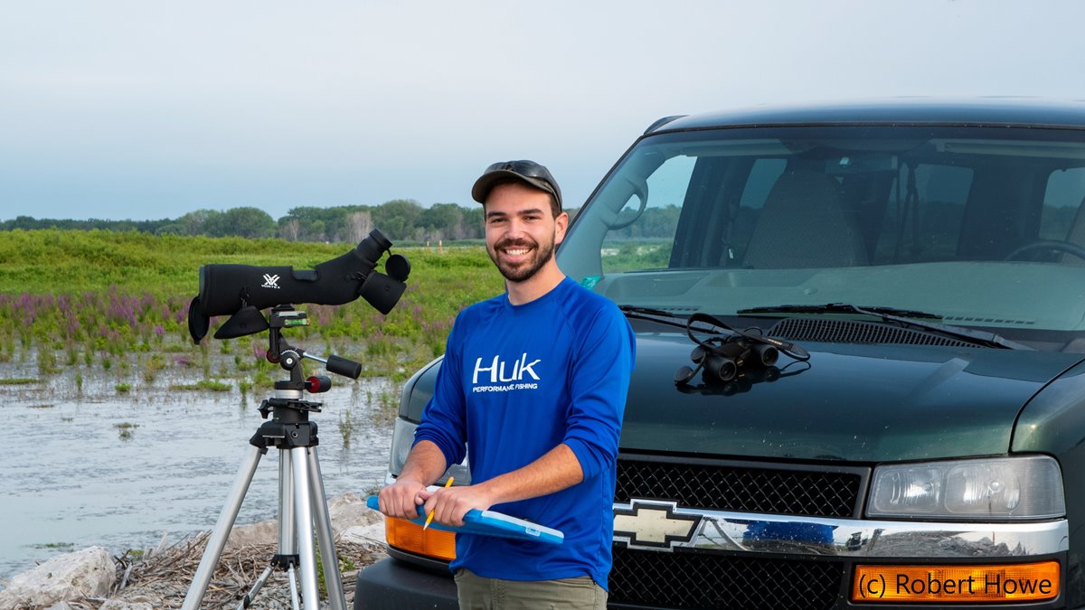 Student with a telescope posing by a car