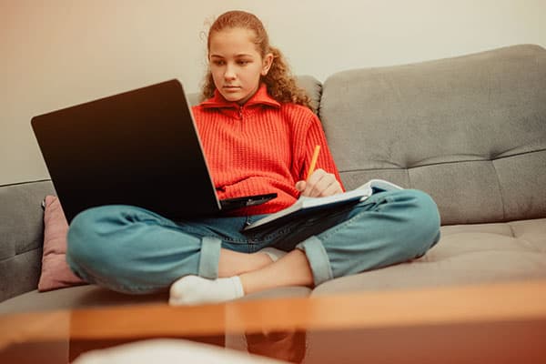 teenage girl sitting on a couch doing distance learning