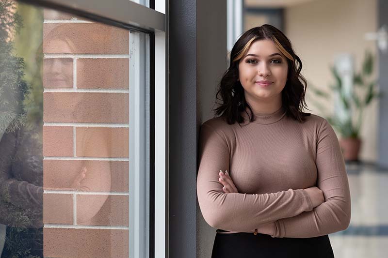 Haley confidently leaning against a wall near a window