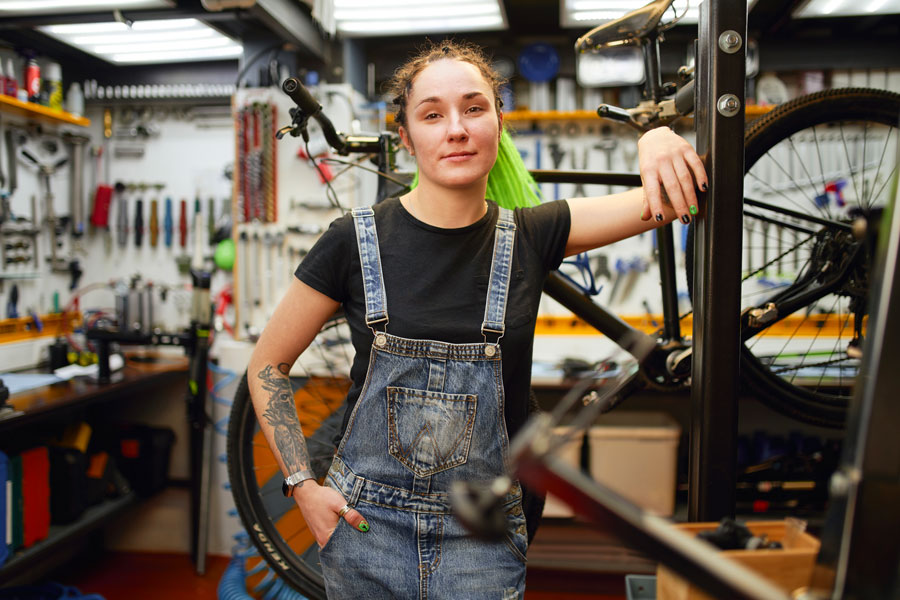 Female with tattoos leans against bike rack in bike shop