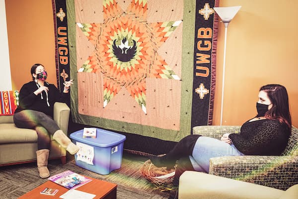 Professor speaks with Indigenous student in front of native quilt
