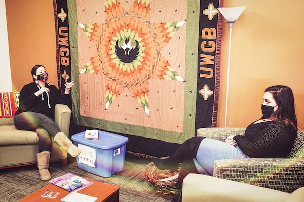 Professor speaks with Indigenous student in front of native quilt