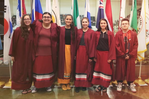 Indigenous students pose in front of flags