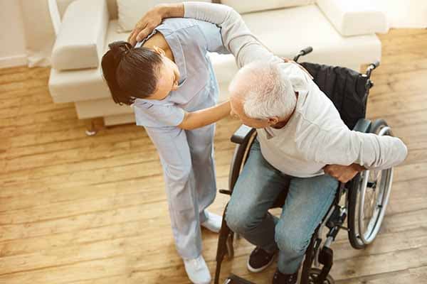 woman caregiver helping man get up from wheelchair