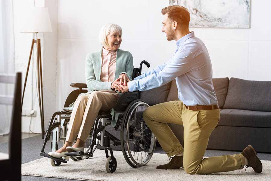 male caregiver kneeling talking with a senior woman