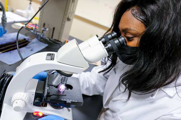 African American female student looks into microscope