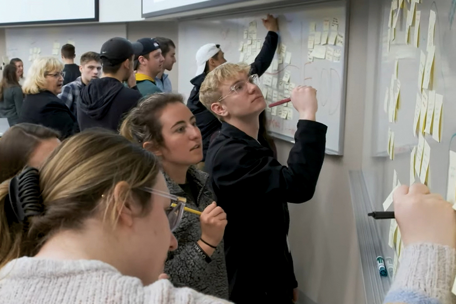 Students writing alongisde sticky notes on a whiteboard