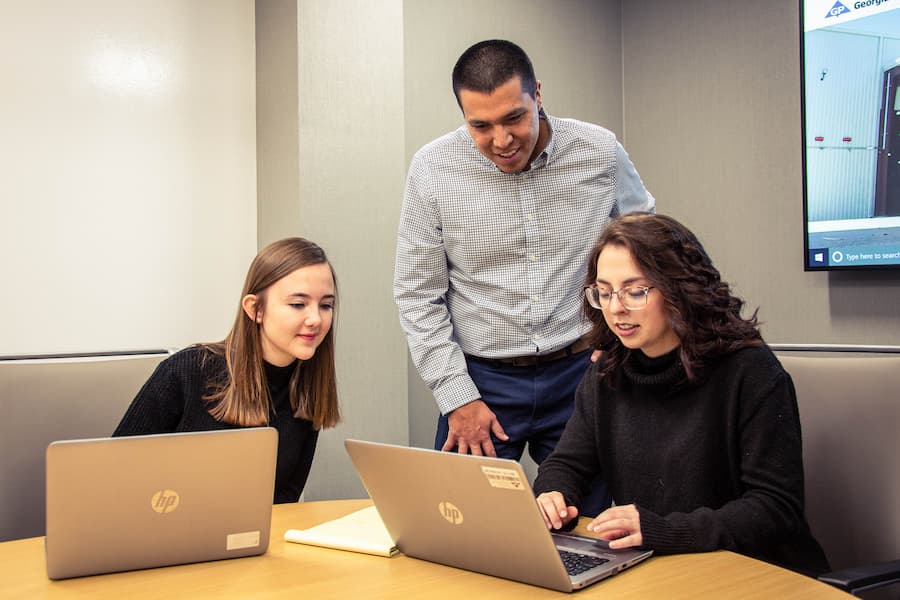 Two students work at desk for Georgia Pacific Intership while supervisor looks on