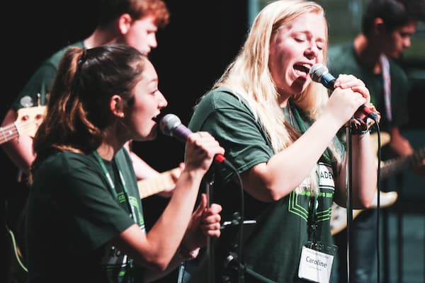 Students sing in to microphones on stage