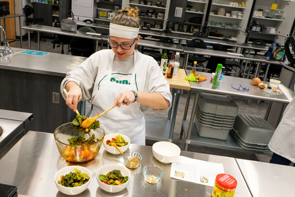 Student mixing salads in industrial kitchen