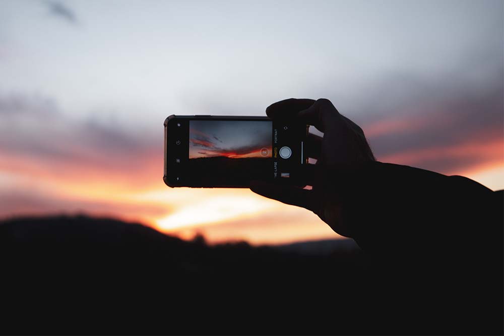 Hands taking a photo of a sunset, phone silhoueted