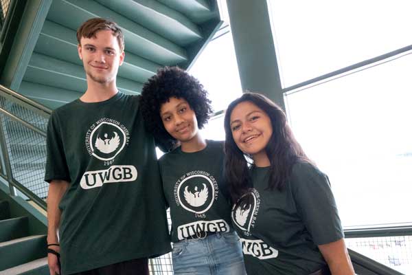 Three students pose on stairs in UWGB t-shrits
