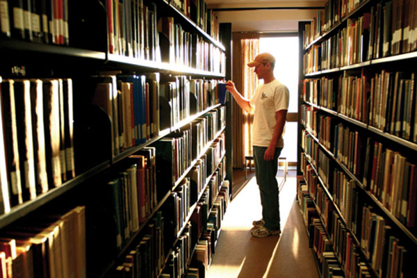 Student selecting a book from the stacks in the Cofrin Library