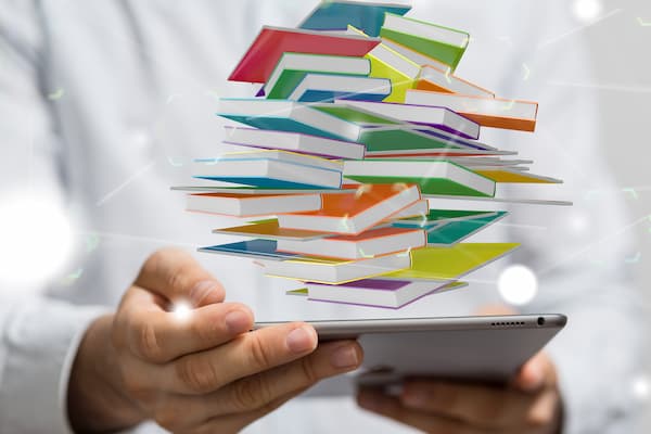 Male holding tablet with stacks of books photoshopped over photo