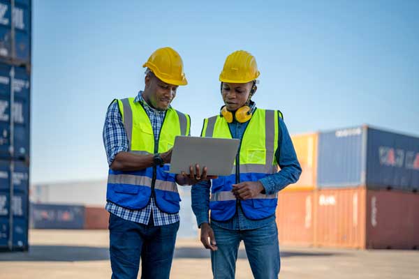 Workers in hard hats look at inventory in shipping yard