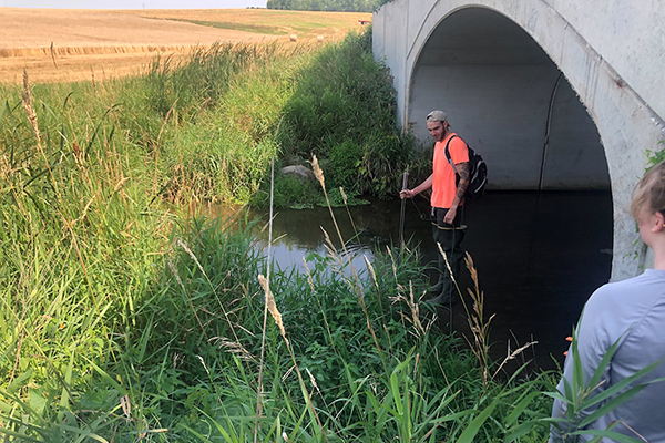 UW-Green Bay Manitowoc student water monitoring a creek near a hay field