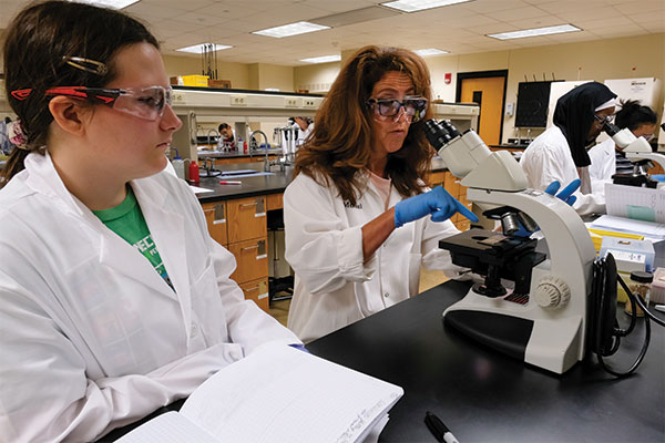 Lisa Merkel helping a student with a microscope.