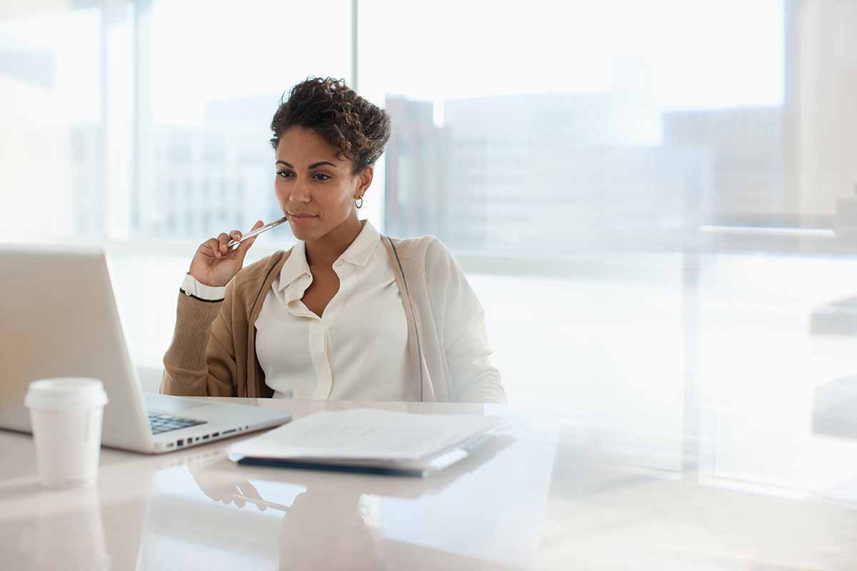 businesswoman using laptop in office with windows behind her