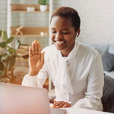woman sitting at laptop waving during virtual meeting