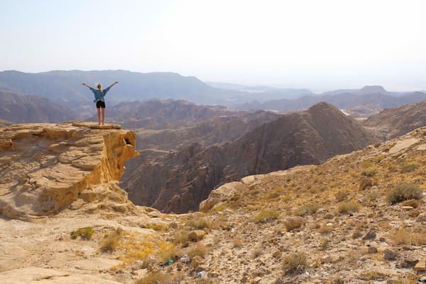 Female standing on a cliff with outstretched arms looking at vast mountainscape