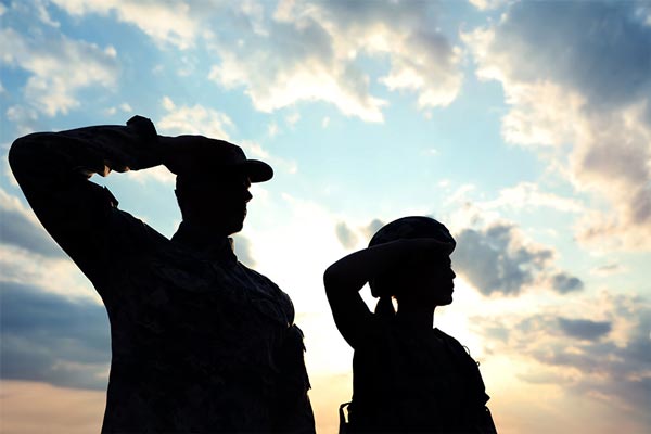 Military service members in uniform saluting sihlouetted by the sky behind them