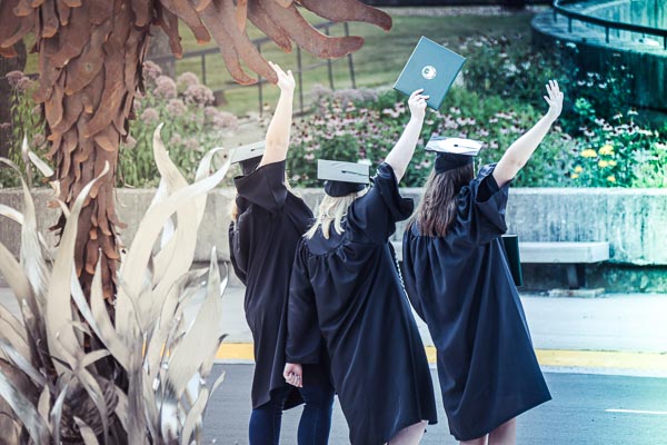 graduates waving in front of the phoenix statue