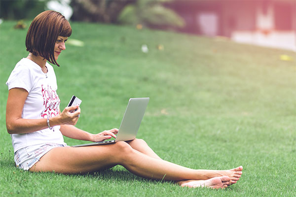 Woman barefoot on lawn, making credit card payment on a laptop.