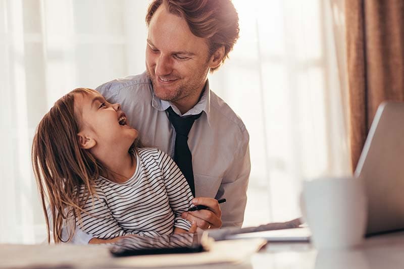 dad smiling looking at daughter sitting by laptop