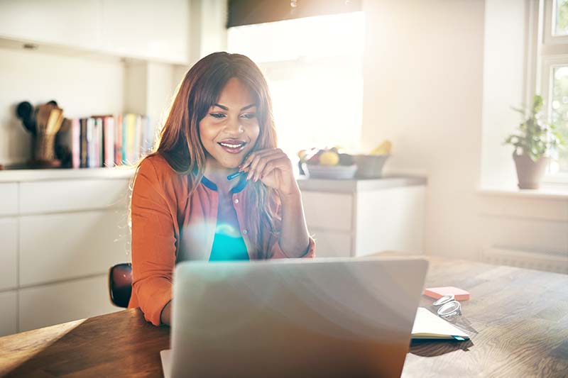 woman looking at laptop screen while sitting at kitchen table