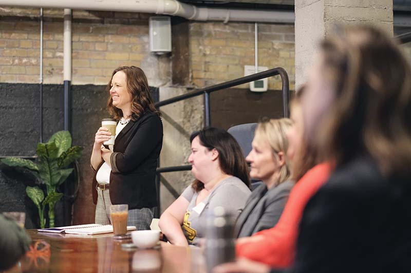 smiling woman standing holding coffee cup during a meeting