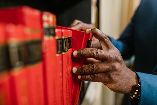 Hands of a person of color pulling out a volume from a bookshelf