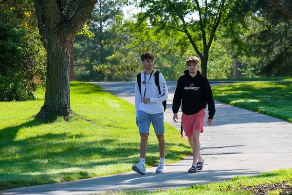 Two students walk among a sunny, green campus