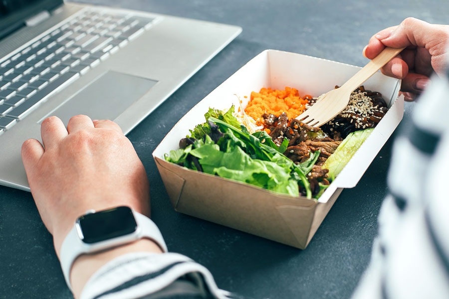 Faculty member working at computer while enjoying lunch