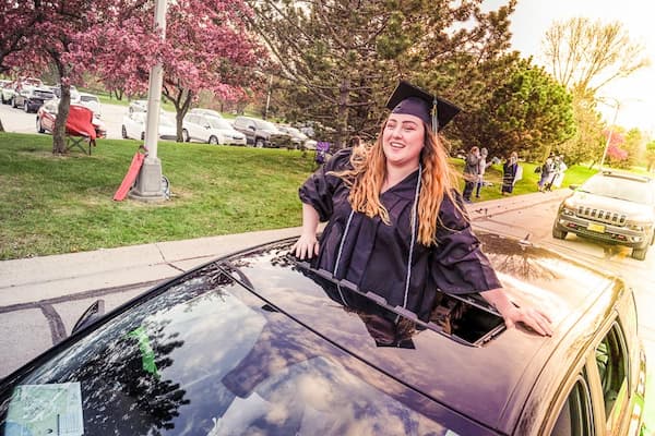 Student stands through sun roof during commencement car parade