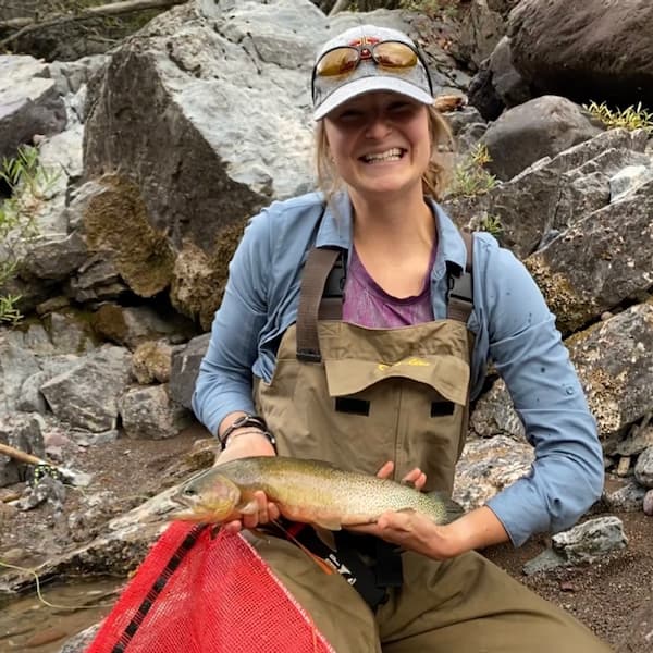 Madeline McKeefry doing field work, holding a trout